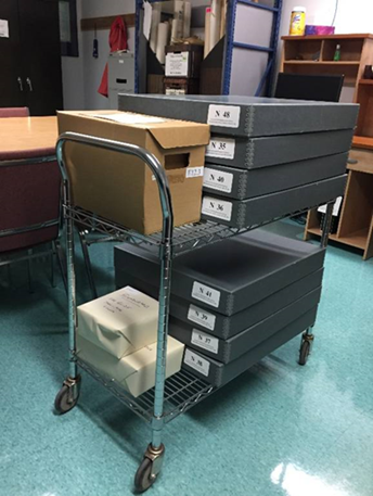 Boxes of microfilm and newspapers on trolley.