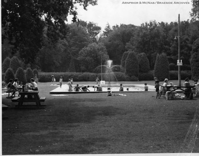 Photograph of the park with citizens at picnic tables, in the fountain and on the grass.