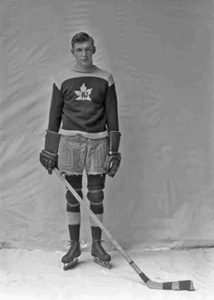Herb Handford dressed in his hockey uniform, wearing his skates and holding a hockey stick.